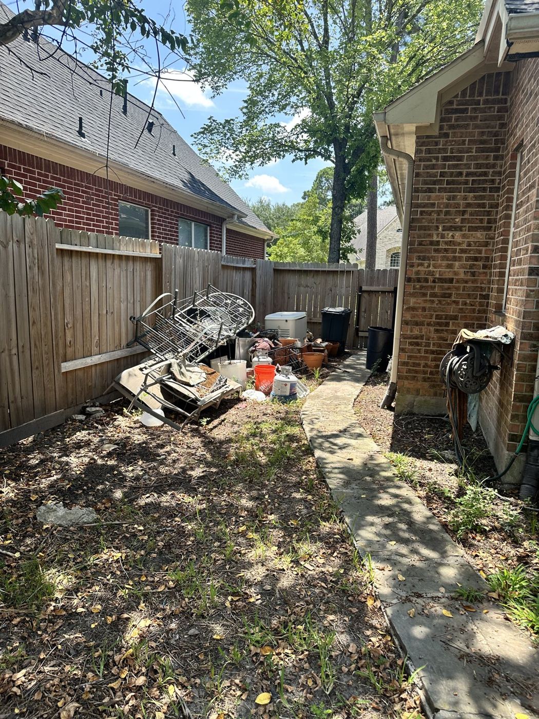 Narrow side yard with old patio furniture and a grill waiting to be hauled